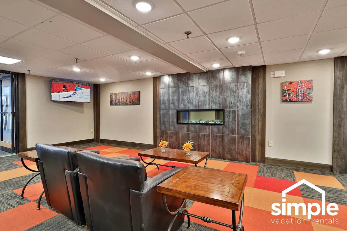 A modern seating area with black armchairs surrounding a coffee table, a cozy fireplace, a television above the mantel, and artwork on the wall. The setting is ideal for socializing, relaxing, or enjoying a quiet moment by the fire after a day of adventure.