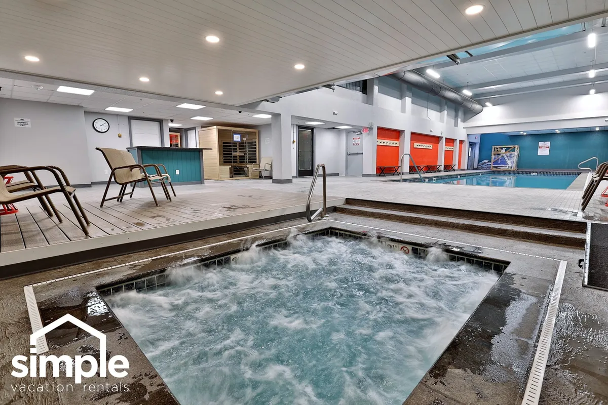 This image features an inviting indoor swimming pool and adjacent hot tub, with comfortable lounge chairs and a locker area nearby. The setting is tranquil and spa-like, illustrating a prime amenity available to guests year-round.