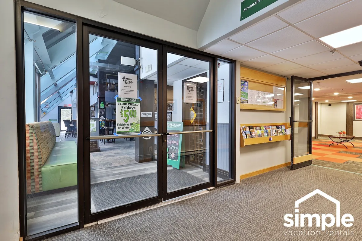 The image shows glass doors opening to a bright, welcoming reception area with an information wall, emphasizing the sense of arrival and access to local attractions or resort grounds.