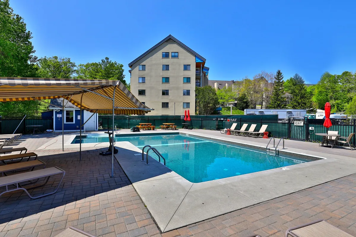 An exterior view of the resort's heated swimming pool surrounded by sun loungers, cabana, and lush greenery, capturing the cheerful mood of summer days spent outdoors. The pool area is inviting and emphasizes seasonal enjoyment.