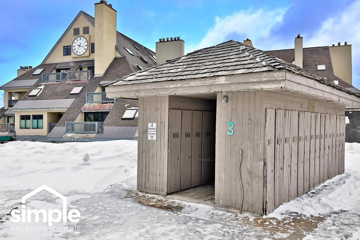 This exterior image showcases a snow-covered ground with a building facade and a clock tower. Lockers are in view, evoking the ski culture and the communal aspect of post-adventure gatherings. People are seen socializing by the lockers, reinforcing the après-ski atmosphere.