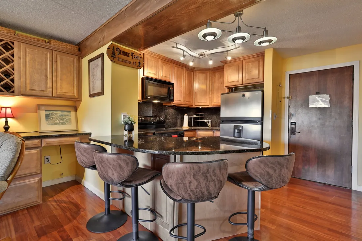 A cozy kitchen area with a prominent island featuring seating, wood cabinetry, and a full suite of appliances. The setup encourages family-style meals, casual dining, and effortless entertaining, reflecting a warm and functional environment.