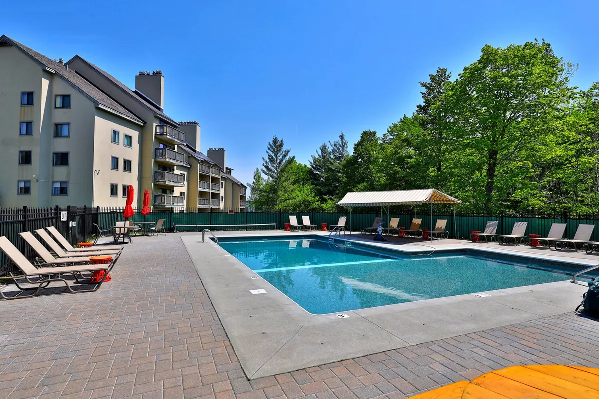 This image features a sparkling swimming pool encircled by comfortable lounge chairs, a cozy cabana, and an abundance of surrounding greenery. The relaxed setup is perfect for sunbathing, social gatherings, or simply enjoying the peaceful mountain air.