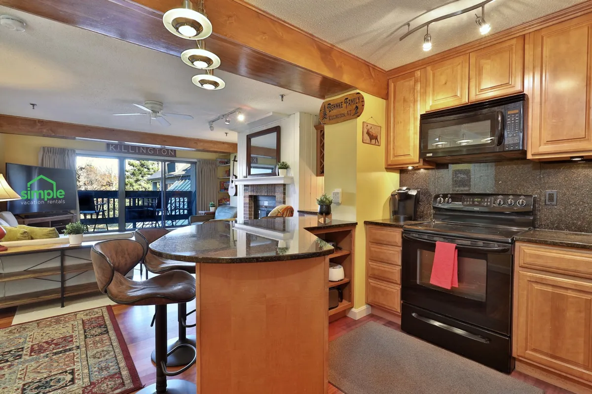 A welcoming kitchen space featuring a central island with bar stools, stainless steel appliances, granite countertops, and an adjacent dining area. The composition highlights an open layout ideal for socializing, with plenty of counter space for preparing and serving meals.