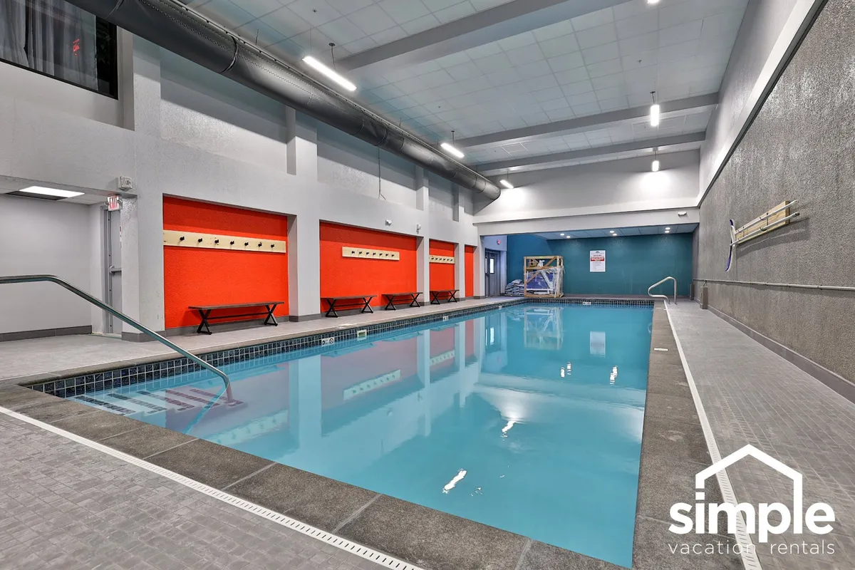 A bright, cheerful indoor swimming pool area with vibrant colored walls and benches lining the poolside. The inviting space is designed for relaxation and socializing after a day outdoors, perfect for unwinding or family fun.
