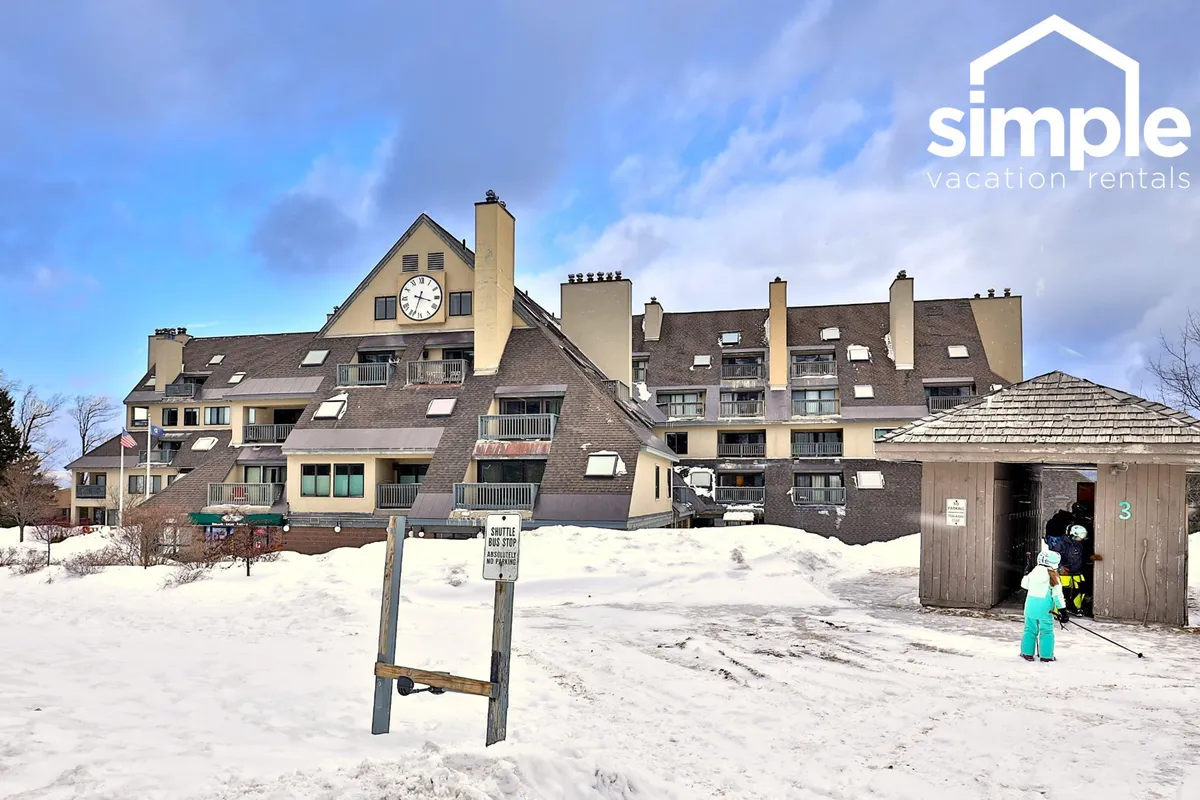 This image features the building facade of the resort, highlighted by a distinctive clock tower and welcoming entranceway. The ground is blanketed in snow, and there's an inviting, cheerful atmosphere, suggesting active winter fun and family gatherings.
