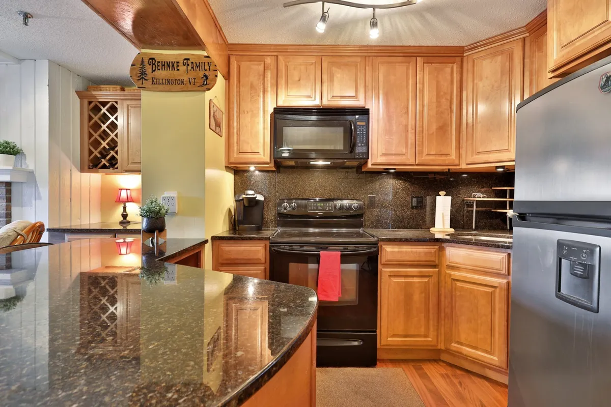 A kitchen scene with granite countertops, wooden cabinets, modern appliances, a wine rack, and a decorative sign. The inviting atmosphere highlights a space suited for both cooking and enjoying coffee or snacks, with thoughtful touches that cater to family needs.